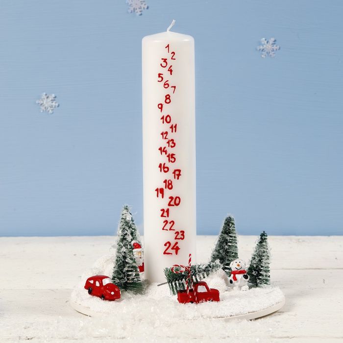 Une décoration avec une bougie de l'Avent entourée d'un monde de Noël miniature