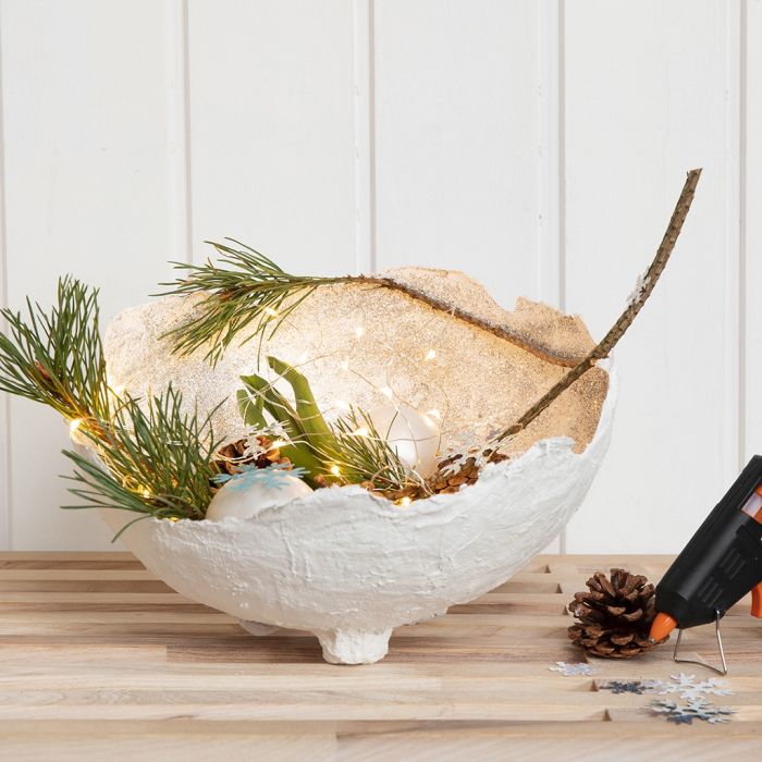 Un bol en bandage de gaze avec des paillettes, décoré avec des boules en verre, des cônes, etc.