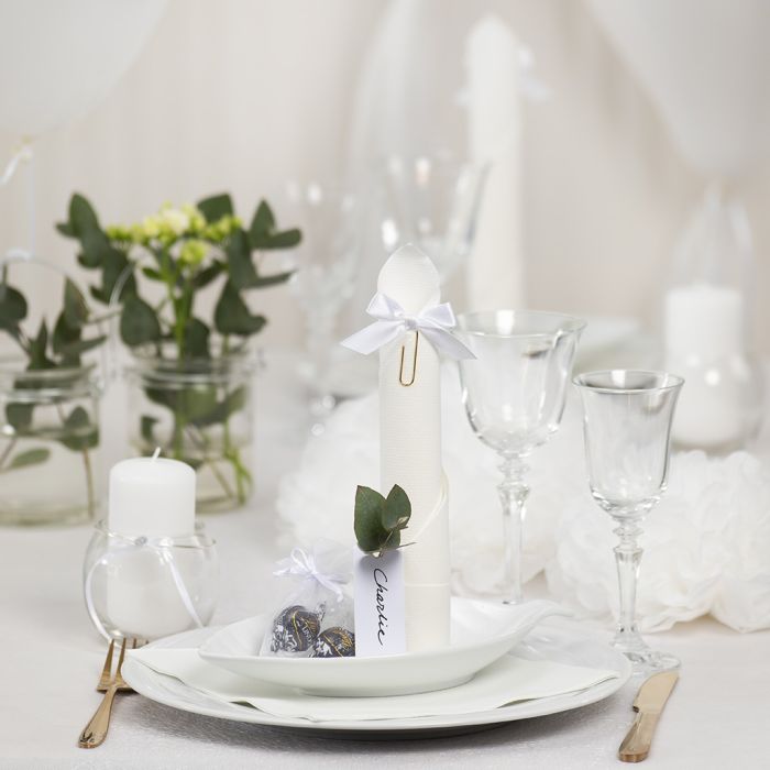 Décorations de table blanches avec des fleurs en papier, des ballons, une serviette pliée en forme de tour et des marque-places.