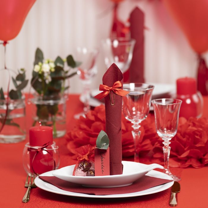 Décorations de table rouges avec des fleurs en papier, des ballons, une serviette pliée en forme de tour et des marque-places.