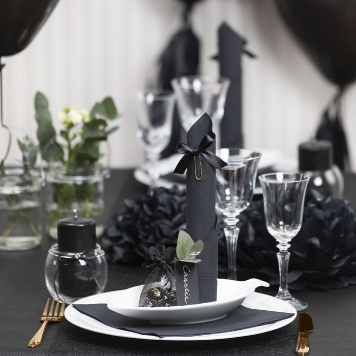 Décorations de table noires avec des fleurs en papier, des ballons, une serviette pliée en forme de tour et des marques-places