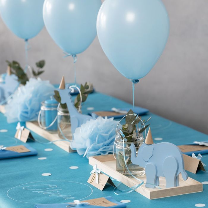 Décorations pour un baptême avec des animaux en bois, des serviettes pliées, des cartes de menu, des pompons et des ballons à l’hélium