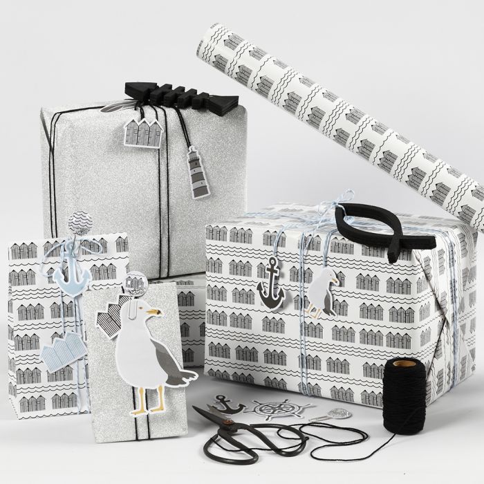 Emballage cadeau noir, blanc et argent pailleté avec des étiquettes cartonnées, des poissons en bois et des pinces métalliques à secouer.