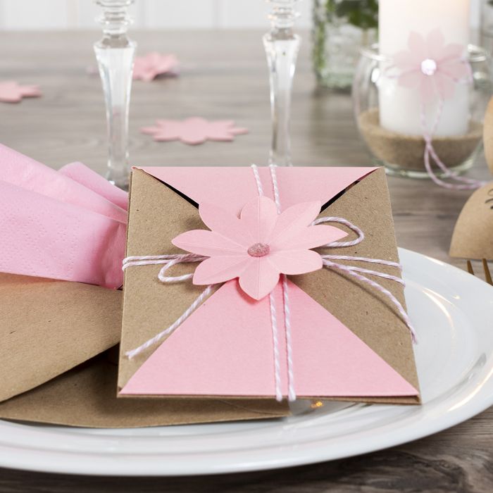 Une invitation emballée et maintenue avec du cordon de coton et une fleur découpée à l’emporte-pièce.