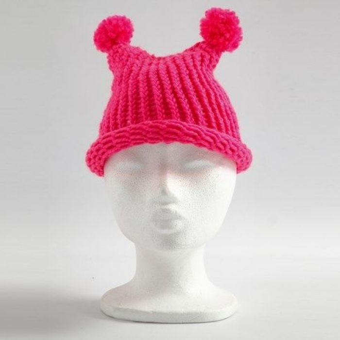 Un bonnet fait avec un métier à tricoter avec deux pompons tricotés