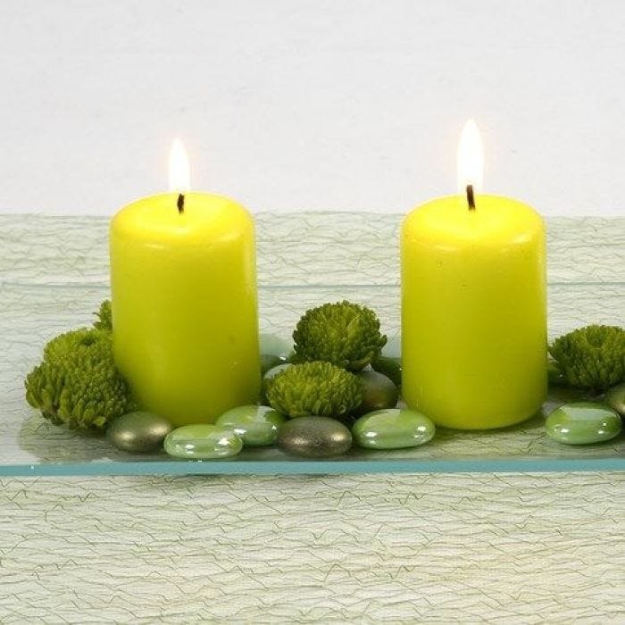 Des bougies vert citron et des pierres décoratives en verre sur un plat en verre
