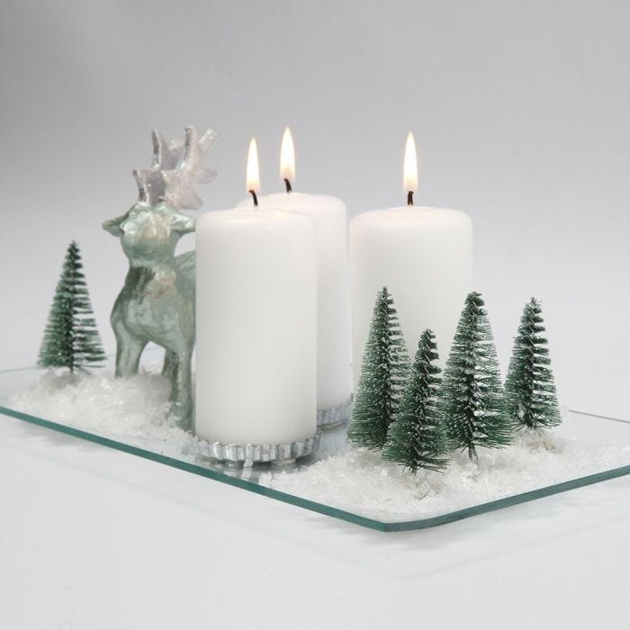 Une décoration de Noël avec de bougies, des rennes, des arbres et de la neige sur un plat en verre