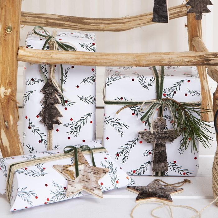 Emballage cadeau de Noël avec un motif de branches vertes, décoré d'un bout de chanvre naturel, d'un ruban et d'une étiquette cadeau en écorce d'arbre