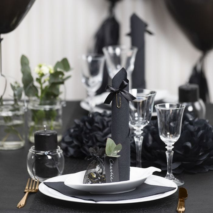 Des décorations de table noires avec des fleurs en papier, des ballons, des serviettes pliées en forme de tours et des marque-places