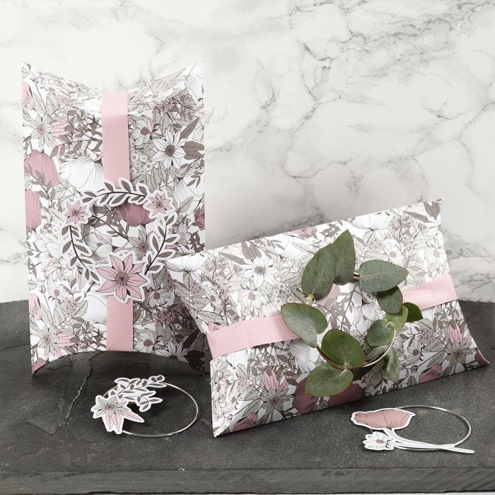 Boîtes cadeaux à plier, décorées avec un ruban rose, un anneau métallique et des découpes de fleurs en papier cartonné