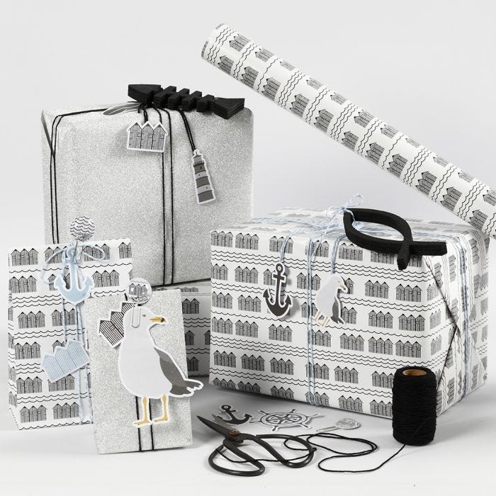 Emballage cadeau noir, blanc et argent pailleté avec des étiquettes cartonnées, des poissons en bois et des pinces métalliques à secouer.