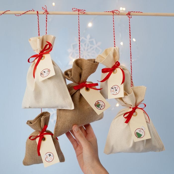 Un calendrier de l'Avent fait avec des sacs en tissu et des numéros autocollants placés sur des étiquettes cadeaux