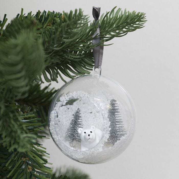 Une boule de Noël avec un orifice sur la face antérieure, décorée de neige artificielle et de mini figurines 