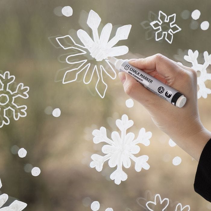 Une fenêtre décorée avec des flocons de neige faits avec des feutres à craie