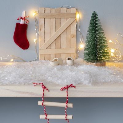Une porte de lutin en bâtonnets de glace avec une échelle en corde et une boîte aux lettres en forme de chaussette de Noël.