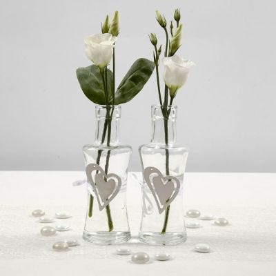 Un vase en verre décoré d'un coeur en bois fixé avec une ceinture en ruban de satin blanc